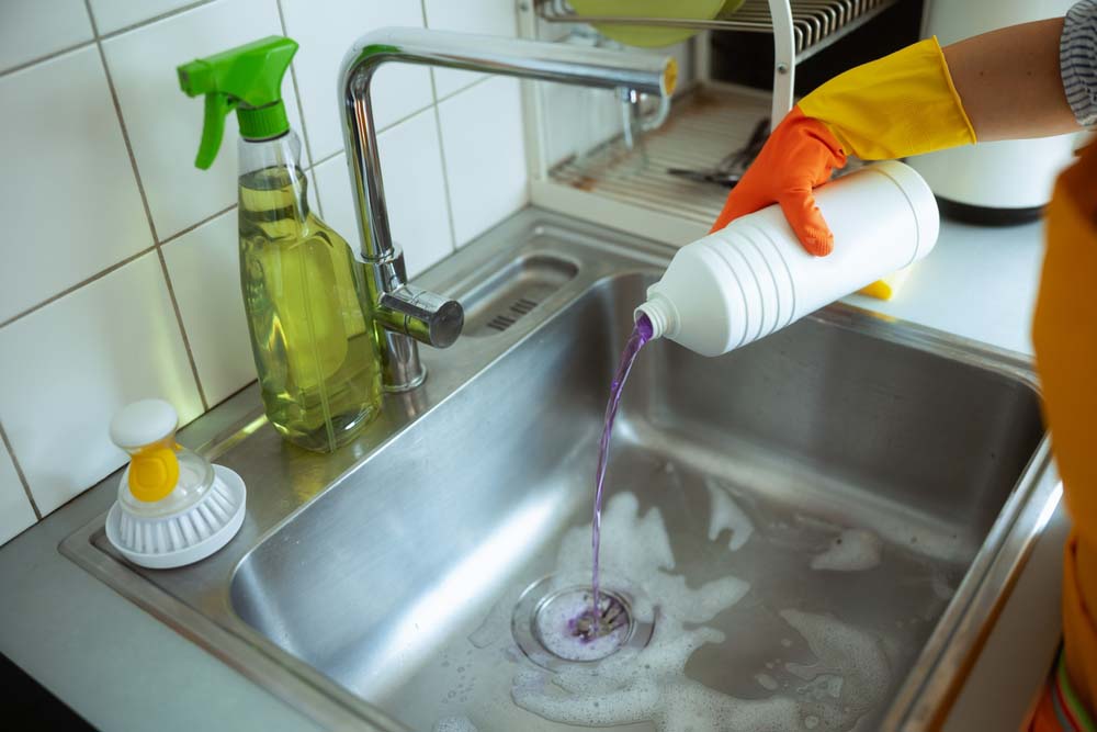 clogged sink drain with harsh chemical bottles nearby